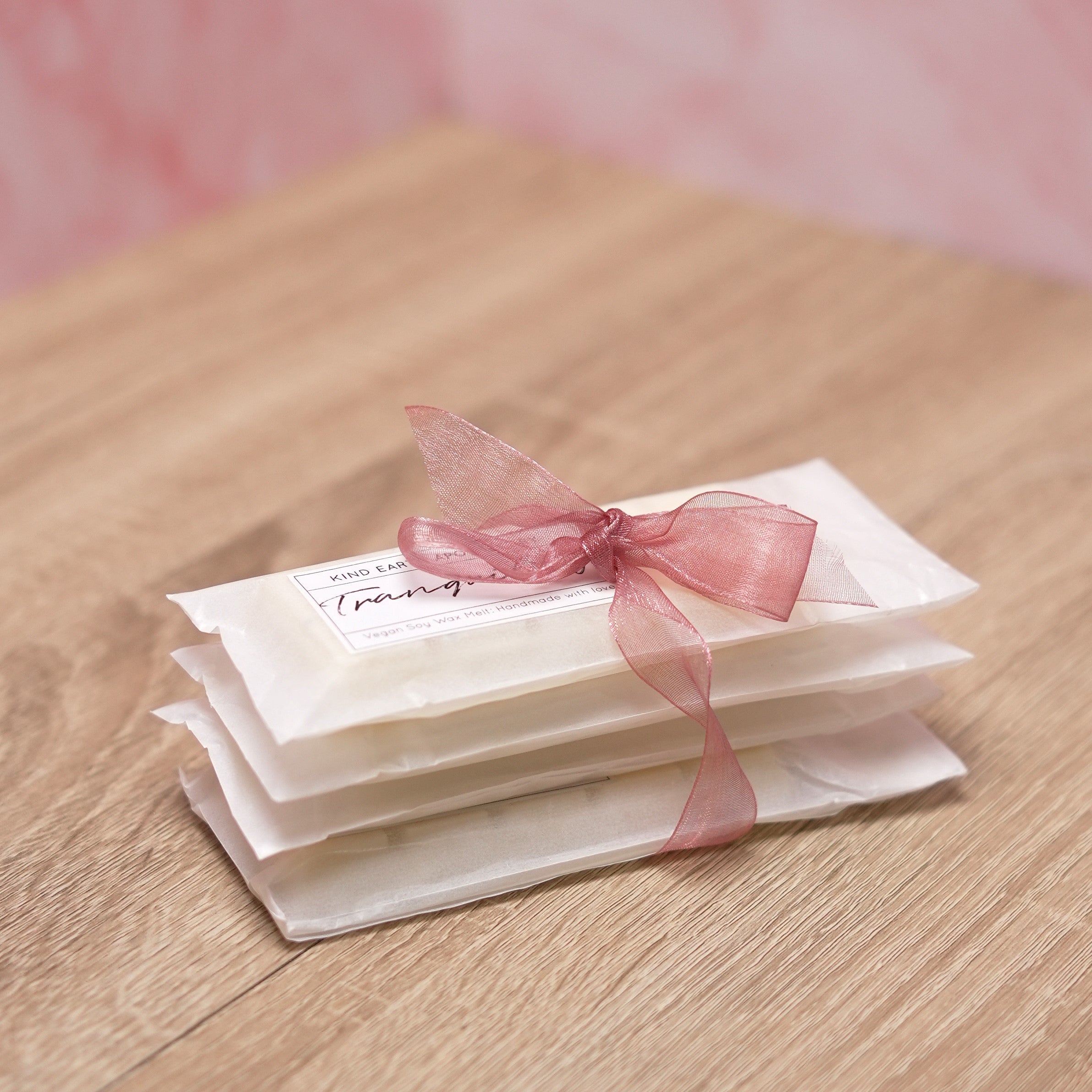 A stack of white rectangular soy wax melts tied with a pink ribbon, with a pink background.