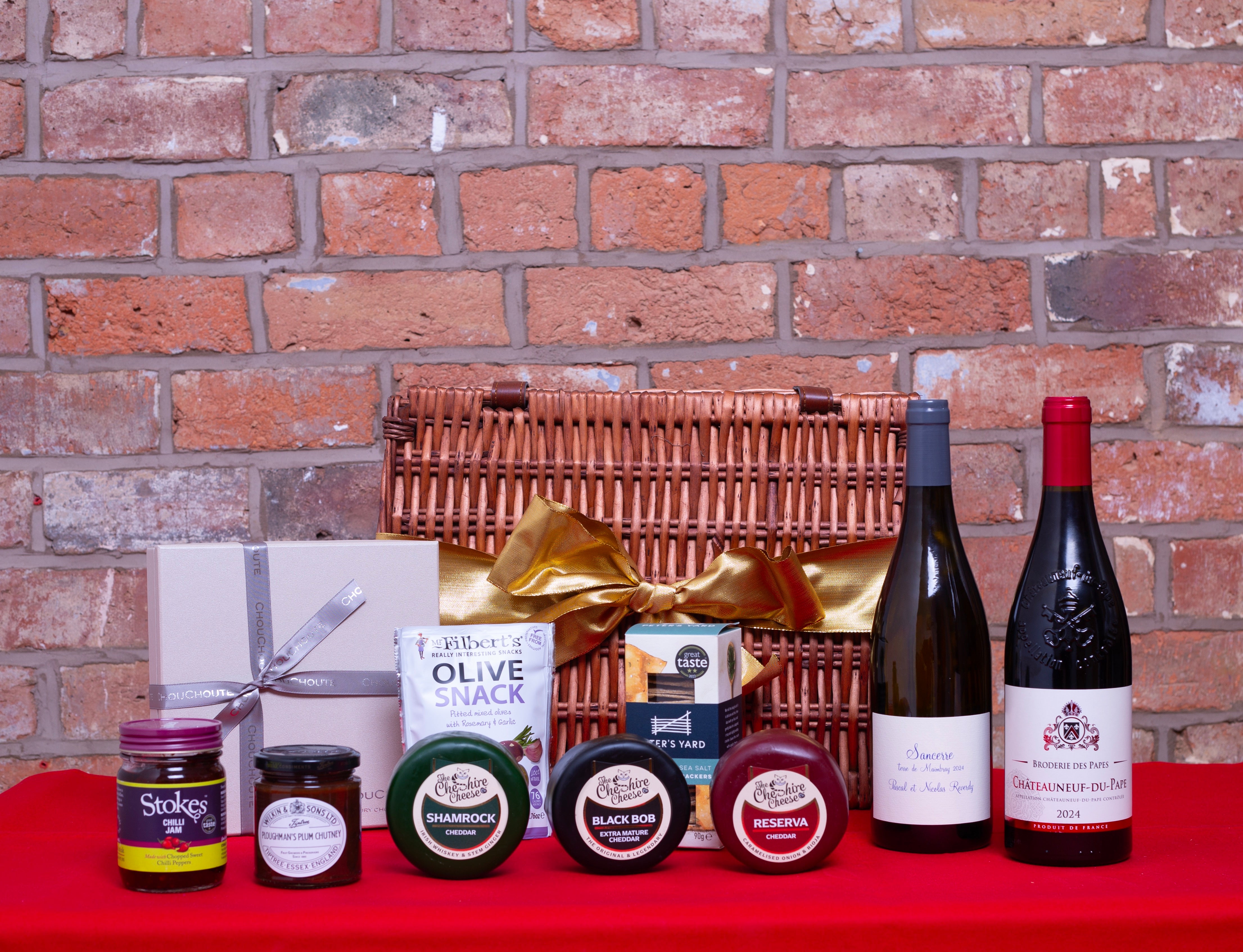 Christmas Wine and cheese gift hamper tied with gold ribbon against a brick wall.