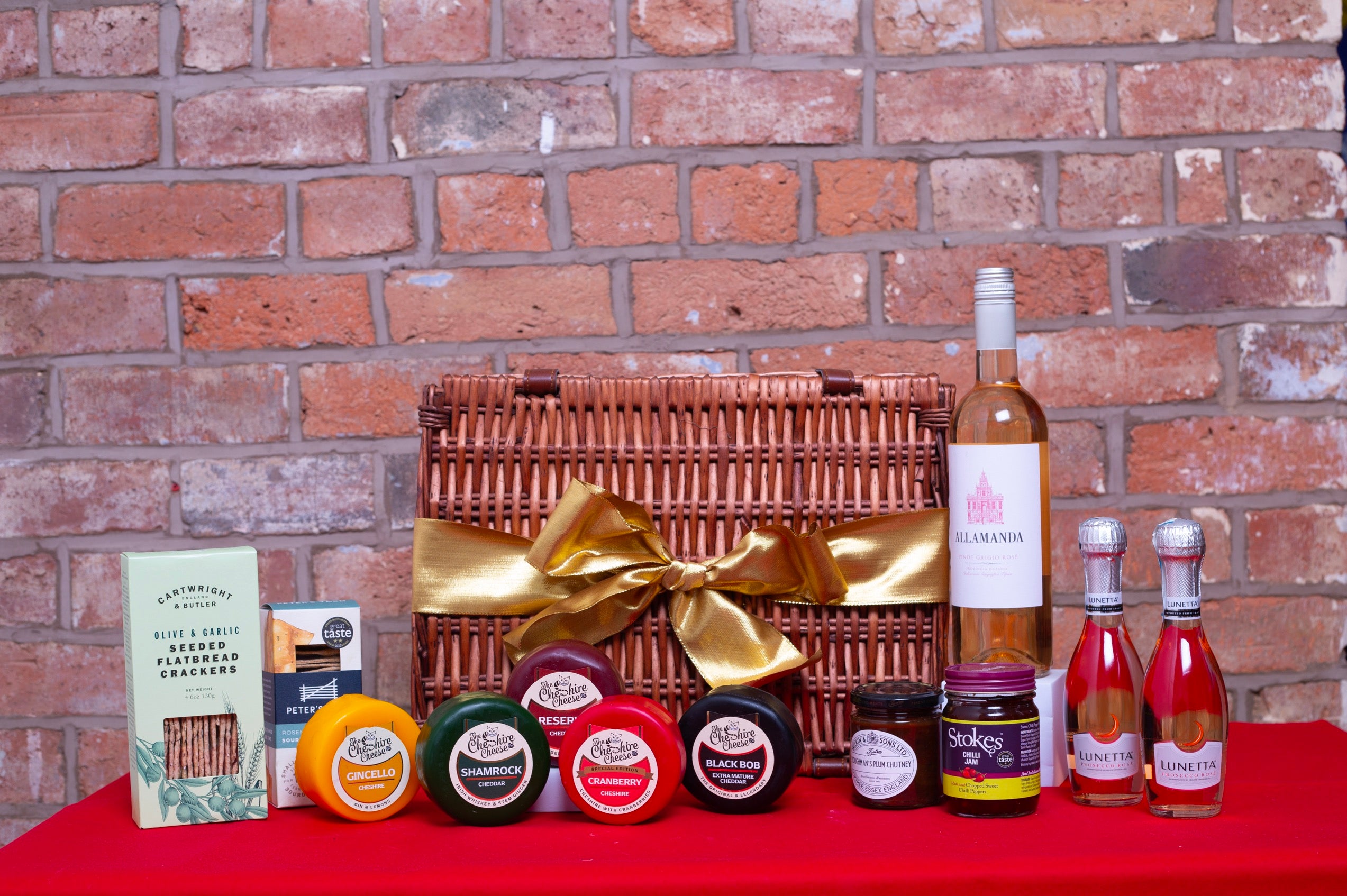 Gourmet gift basket with wine, jams, and other items against a brick wall.