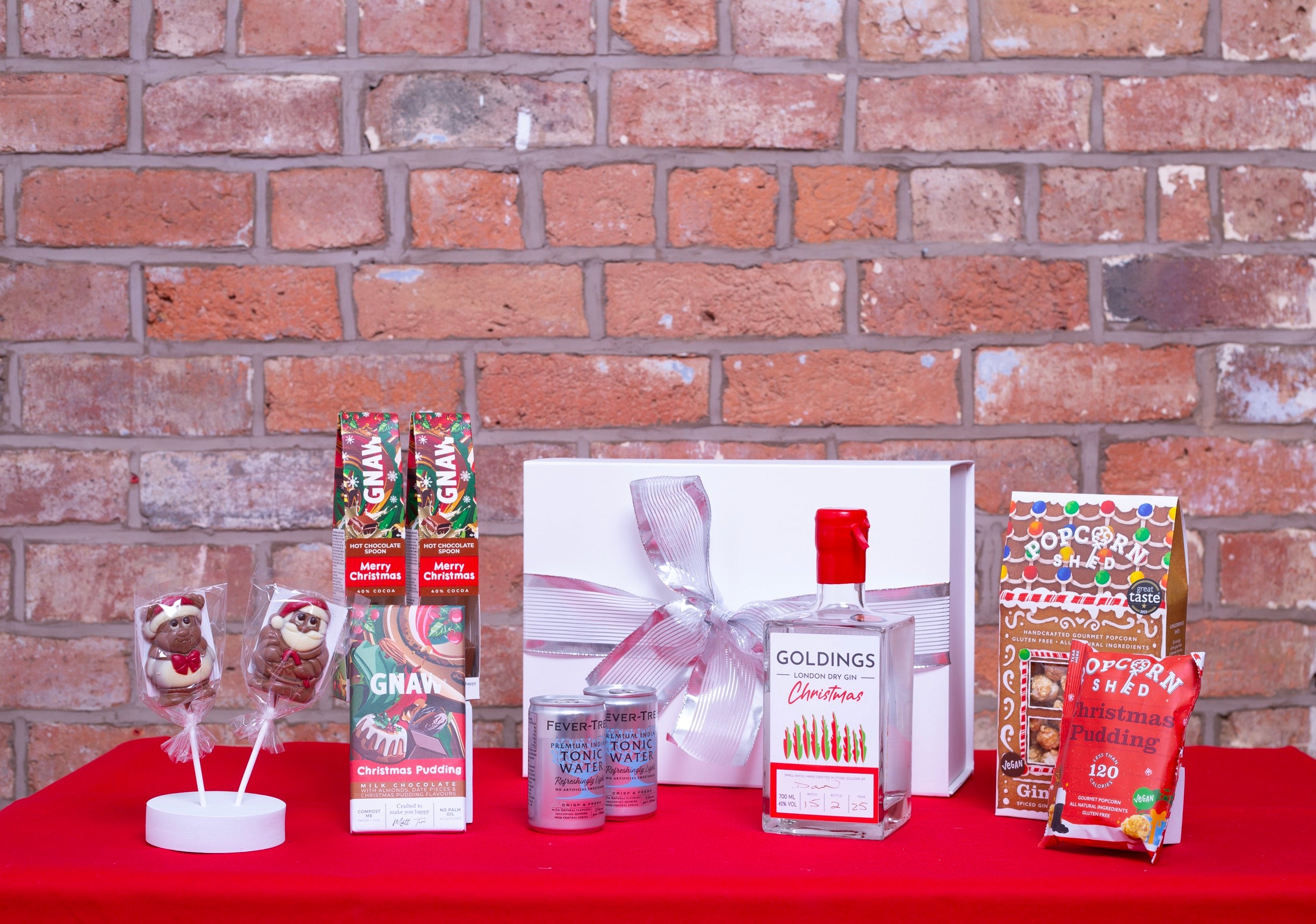 A white gift box with silver ribbon and a selection of Christmas chocolate treats with a Christmas gin