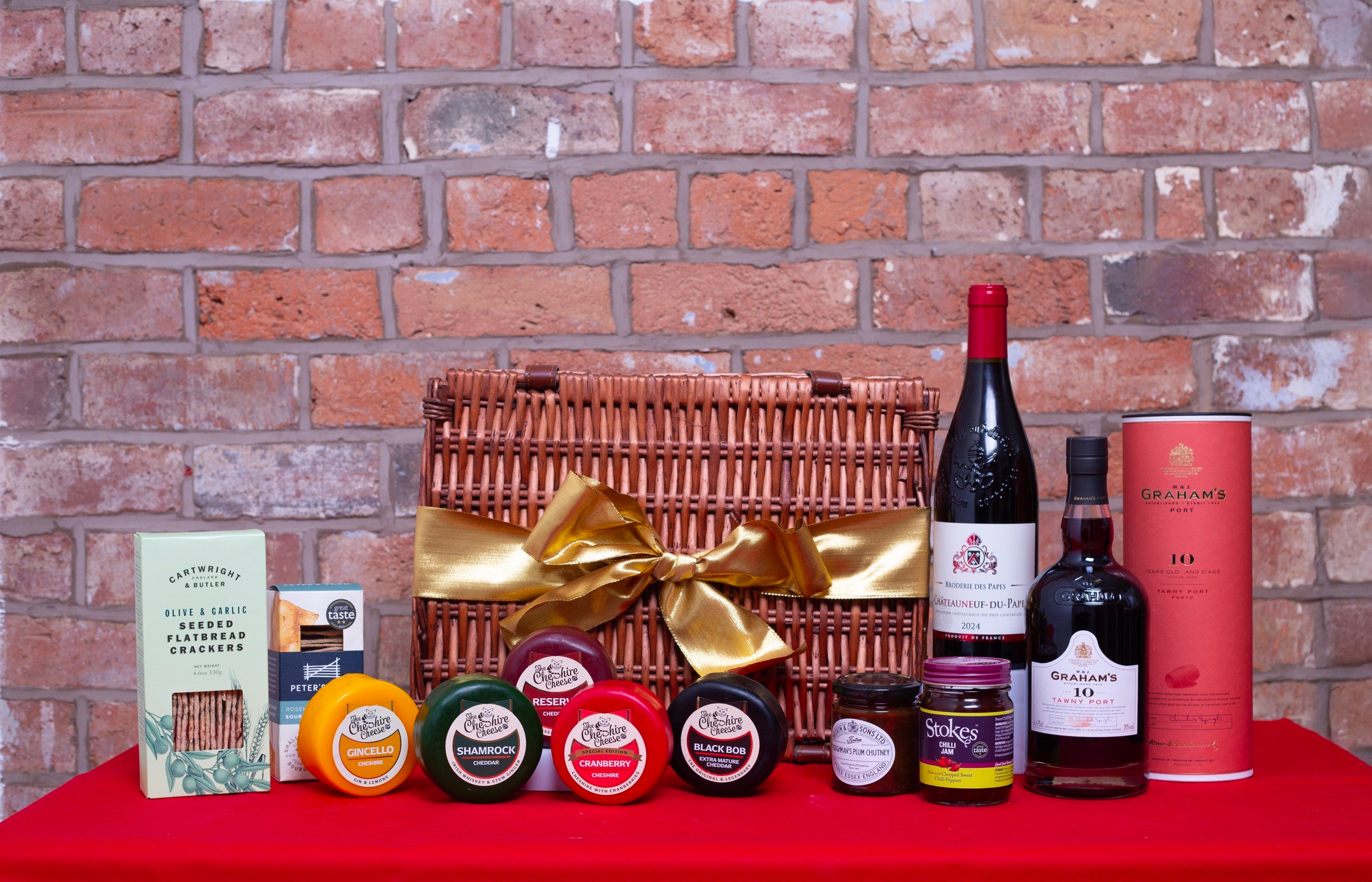 Wine gift set with a basket, bottles, and jars against a brick wall.