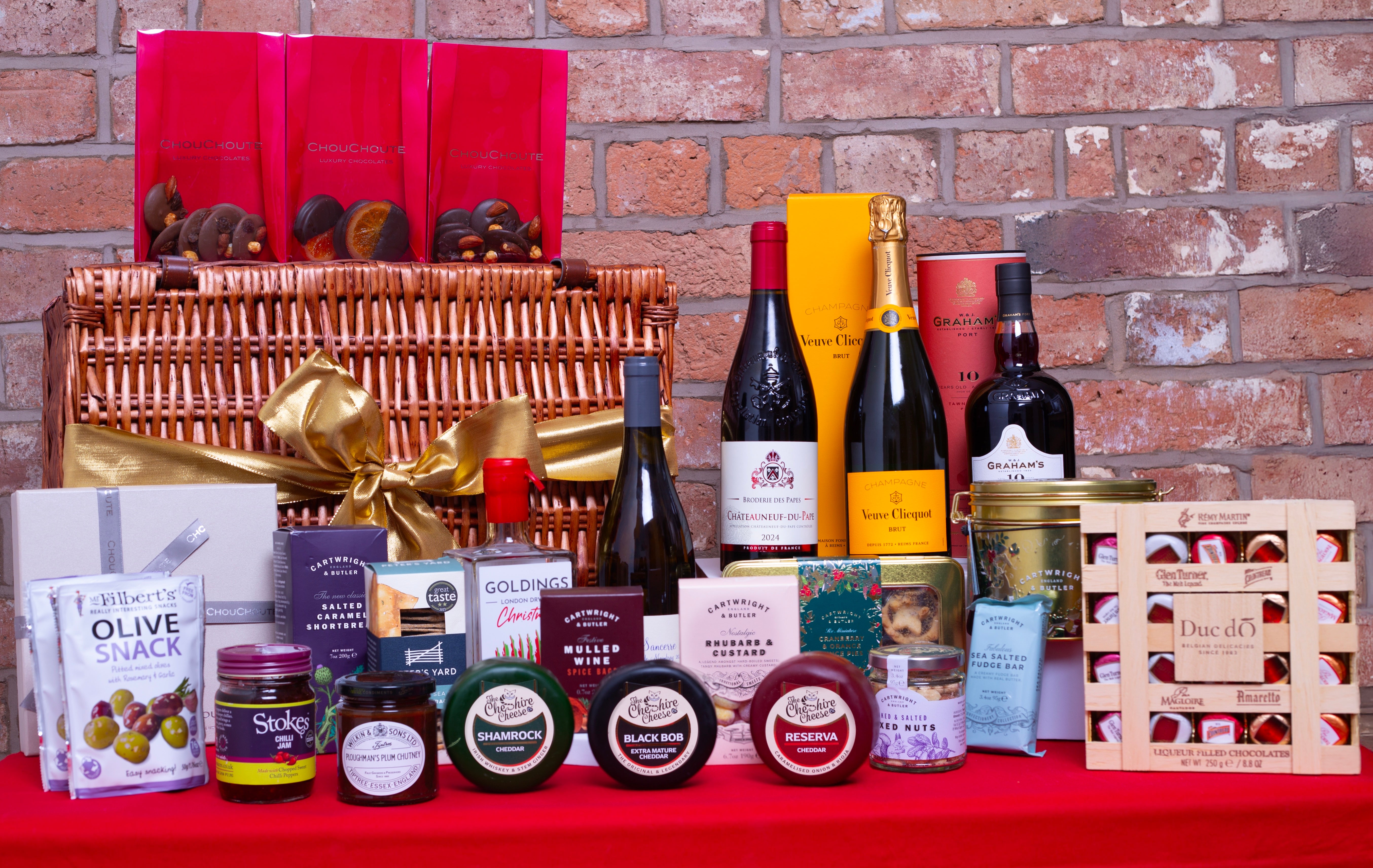 Assorted gourmet food and wine items on a red surface with a brick wall background Christmas Hamper 