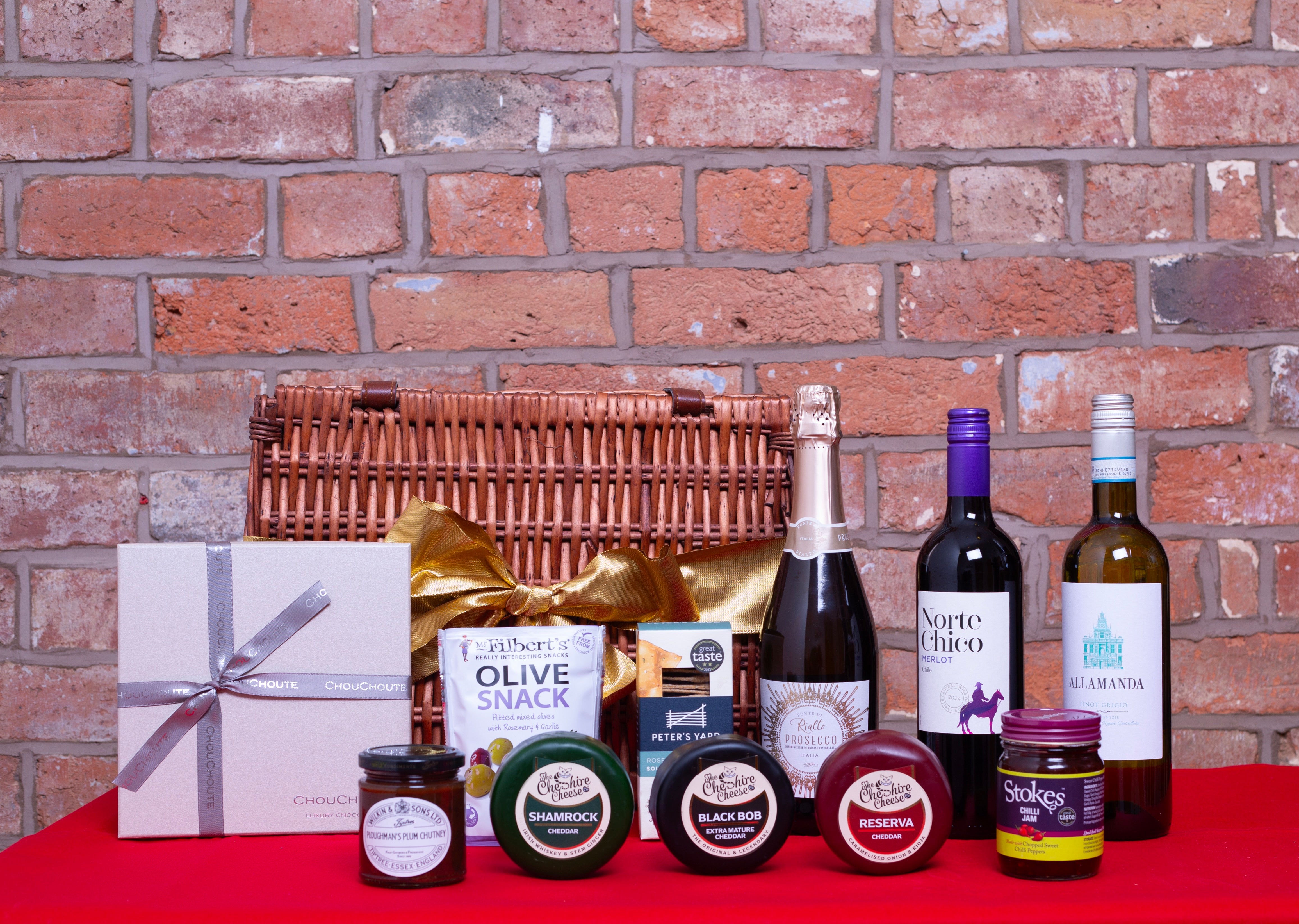 Gift basket with wine, cheese, and other items against a brick wall.